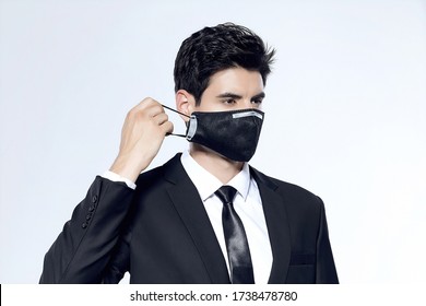 The Young Office Man Removes The Black N95 Medical-surgical Mask He's Wearing Against A White Background.