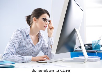 Young office worker staring at computer screen and adjusting glasses.