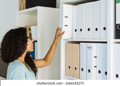 Young office worker taking a file or large binder from the shelf with a smile in a profile view