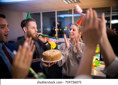 Young Office Workers Congratulating Female Colleague On Birthday, Holding Cake And Blowing Party Horns