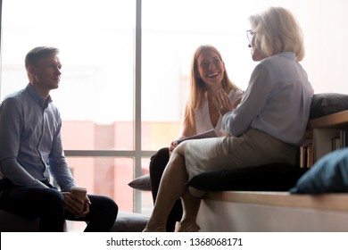 Young Office Workers Interns Listening To Old Woman Mentor Coach Talking To Team People At Meeting, Mature Female Business Leader Boss Chatting With Employees Having Fun Conversation At Work Break