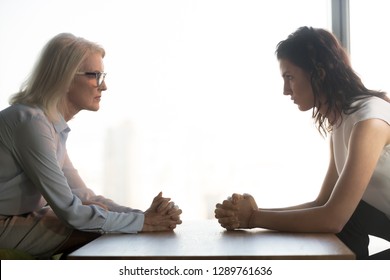 Young And Old Businesswomen With Clasped Hands Looking At Each Other Sitting Opposite As Rivalry Confrontation Concept, Female Career Success Envy And Jealousy, Generations Conflict At Work Concept