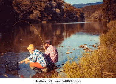 Young and old fisherman standing on the shore of lake with fishing rod. Father and son enjoy life. Men family, granddad and drandson fishing. Mature man fisher celebrate retirement. - Powered by Shutterstock