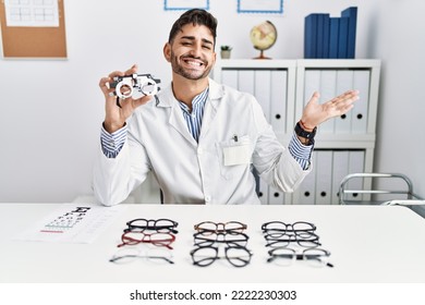 Young Optician Man Holding Optometry Glasses Pointing Aside With Hands Open Palms Showing Copy Space, Presenting Advertisement Smiling Excited Happy 