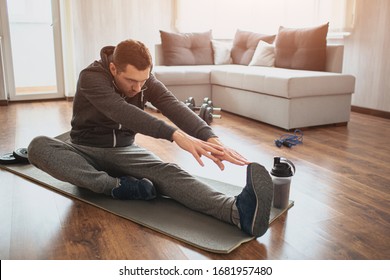 Young ordinary man go in for sport at home. Freshman or beginner stretching with tow hands to one leg. Excercising alone in empty apartment. Try to keep fit and stay healthy with good body - Shutterstock ID 1681957480