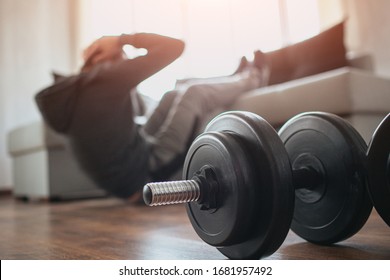 Young ordinary man go in for sport at home. Cut view of a beginner or freshman in workout activity at his apartment. dumbbells on pictures lying on floor. Trying to get better shape - Shutterstock ID 1681957492