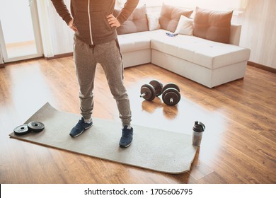 Young ordinary man go in for sport at home. Ordinary freshman in workout stand on mat and hold hands on hips. Cut view of man's low part of regular body. Warming body up. - Shutterstock ID 1705606795