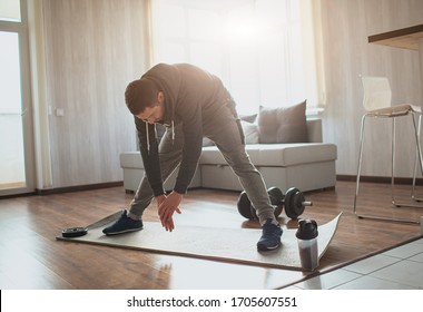 Young ordinary man go in for sport at home. Adult male person stretching down to his feet with hands. Warm up body before first training. Freshman and beginner in action.