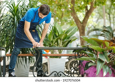 Young Outdoor Cafe Waiter Cleaning Tables With Disinfecting Detergent Before Opening