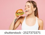 Young overjoyed cool woman wears white top casual clothes hold eat bite burger close eyes isolated on plain pastel light pink background. Proper nutrition healthy fast food unhealthy choice concept