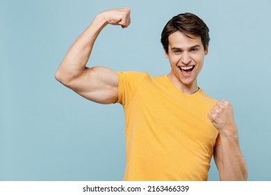 Young overjoyed excited exultant jubilant man 20s wear yellow t-shirt doing winner gesture celebrate clenching fists say yes isolated on plain pastel light blue background studio portrait.