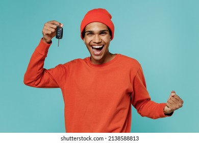Young overjoyed fun excited happy african american man 20s in orange shirt hat hold car key do winner gesture isolated on plain pastel light blue background studio portrait. People lifestyle concept