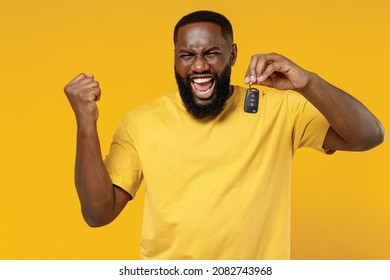 Young overjoyed happy black man 20s wearing bright casual t-shirt hold car key fob keyless system do winner gesture isolated on plain yellow color background studio portrait. People lifestyle concept