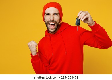 Young overjoyed happy caucasian man wear red hoody hat look camera hold car key fob keyless system do winner gesture isolated on plain yellow color background studio portrait. People lifestyle concept - Shutterstock ID 2254053471