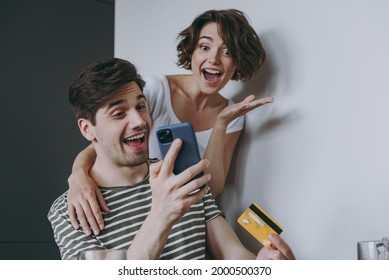 Young Overjoyed Surprise Couple Two Woman Man In Casual Clothes Sit By Table Eat Pancake Use Mobile Cell Phone Credit Bank Card Shop Online Order Delivery In Light Kitchen At Home Healthy Diet Concept