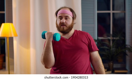 Young Overweight Man Lifting Dumbbell Training Home. Portrait Of Fat Guy Doing Exercises With Sports Equipment In Living Room. Man Losing Weight And Working Out