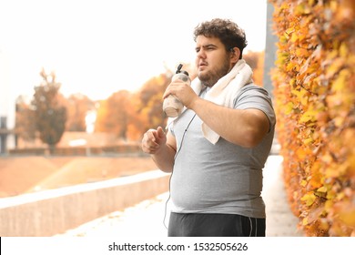 Young overweight man with towel and bottle of water in park