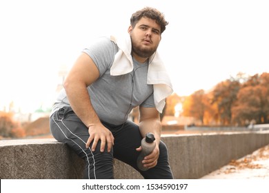 Young overweight man with towel resting in park