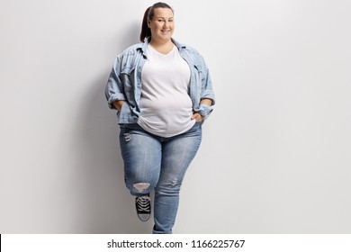 Young overweight woman in casual clothes standing against a wall