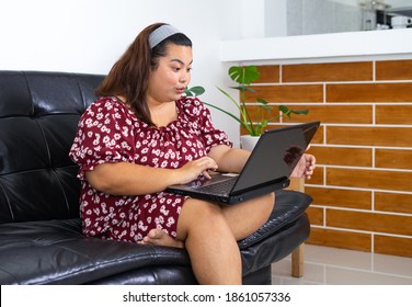 Young Overweight Woman Sitting On The Couch And Using Laptop For Shopping Online. Concept Compulsive Shopping  Retail Therapy Addiction. Happy Working From Home. Shopping Online.