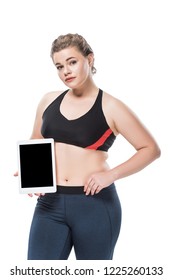 Young Overweight Woman In Sportswear Holding Digital Tablet With Blank Screen And Looking At Camera Isolated On White 