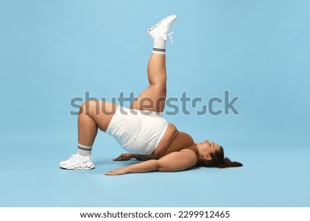 Young overweight woman training in sportswear against blue studio background. Trying hard to lose weight, full-body workout. Concept of sport, body-positivity, weight loss, body and health care