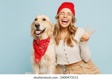 Young owner woman wear casual clothes red hat bandana hug cuddle embrace her best friend retriever dog show v-sign gesture isolated on plain pastel blue background studio. Take care about pet concept