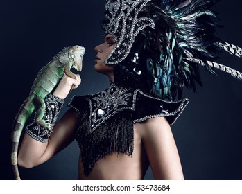 Young Pagan Priest In Ritual Suit With Green Iguana In His Hands. Photo.