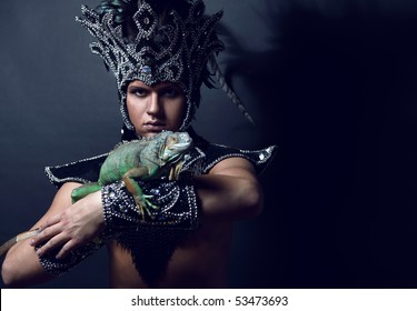 Young Pagan Priest In Ritual Suit With Green Iguana In His Hands. Photo.