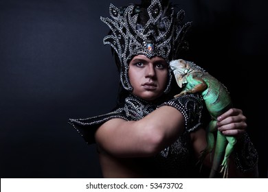 Young Pagan Priest In Ritual Suit With Green Iguana In His Hands. Photo.