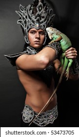 Young Pagan Priest In Ritual Suit With Green Iguana In His Hands. Photo.