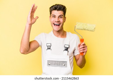 Young painter man isolated on yellow background receiving a pleasant surprise, excited and raising hands. - Shutterstock ID 2115462863