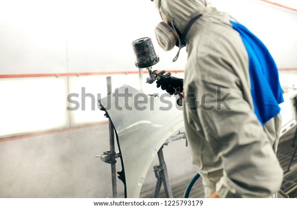 young painter Man with protective\
clothes and mask painting car detail using spray\
compressor