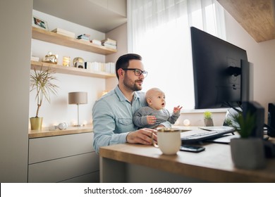 Young parent working from home while holding his baby boy on his lap while they both watch to the screen.