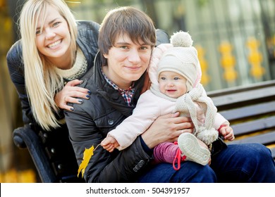 Young Parents With Baby On Bench In Autumn Park