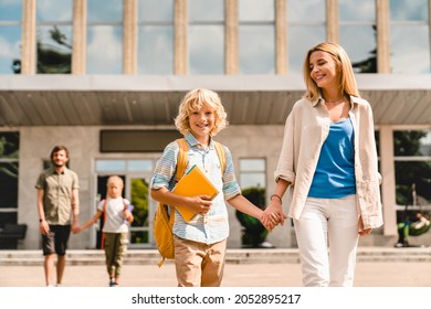 Young Parents Escorting Their Kids Children From School Home After Lessons Classes After Summer Holidays. Welcome Back To School. New Academic Educational Year Semester