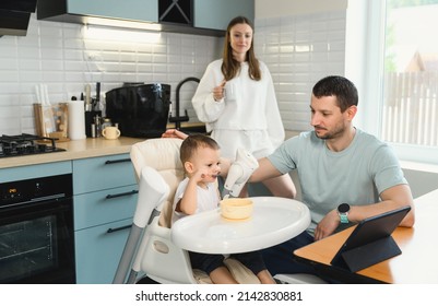 Young parents father and mother feeding the baby. Child on a highchair in the kitchen. Dad, mom and baby - happy full family