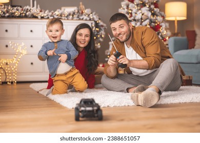 Young parents having fun playing with their toddler boy while spending Christmas day together at home, child excited about Christmas present toy car - Powered by Shutterstock