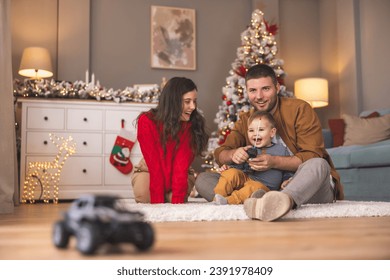 Young parents having fun playing with their toddler boy while spending Christmas day together at home, father teaching son how to use remote controlled toy car - Powered by Shutterstock