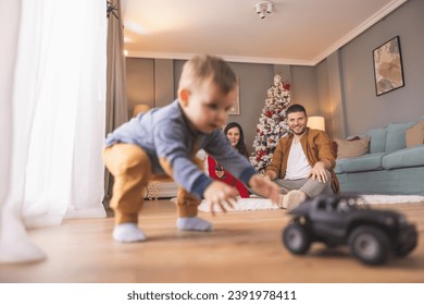 Young parents having fun playing with their toddler boy while spending Christmas day together at home, child chasing remote controled toy car - Powered by Shutterstock