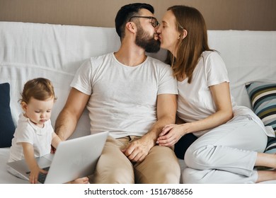 Young Parents Kissing While Their Kid Looking At The Screen Of Computer And Typing, Close Up Photo, Lifestyle, Warm And Tender Feeling And Emotion