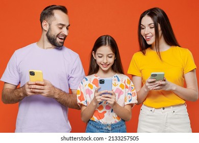 Young Parents Mom Dad With Child Kid Daughter Teen Girl In Basic T-shirts Hold In Hand Use Mobile Cell Phone Peep Isolated On Yellow Background Studio Portrait Family Day Parenthood Childhood Concept