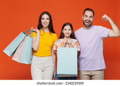 Young Parents Mom Dad With Child Kid Daughter Teen Girl In Basic T-shirts Holding Package Bags With Purchases After Shopping Do Winner Gesture Isolated On Yellow Background Studio Family Day Concept.