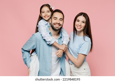 Young parents mom dad with child kid daughter teen girl in blue clothes giving piggyback ride to kid, sit on back isolated on plain pastel light pink background Family day parenthood childhood concept