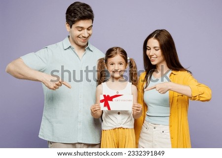 Young parents mom dad with child kid girl 6 years old wear blue yellow casual clothes hold point on store gift certificate coupon voucher card isolated on plain purple background. Family day concept
