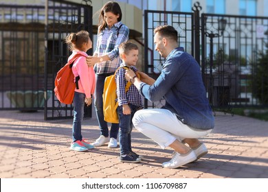 Young Parents Saying Goodbye To Their Little Children Near School