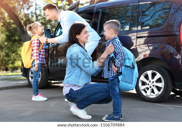 Young parents saying goodbye to their little\
children near school