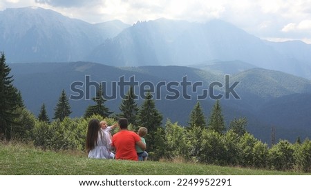 Young parents sitting, holding children and admiring mountains peak landscape