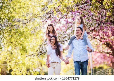 Young Parents With Small Daugthers Walking Outside In Spring Nature.