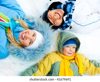 Young Parents And Their Son Wearing Warm Winter Clothes Lie On The Snow